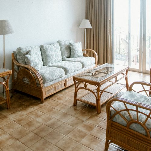 A cozy living room with wicker furniture, floral cushions, two lamps, and a glass-topped table, near a sliding glass door.