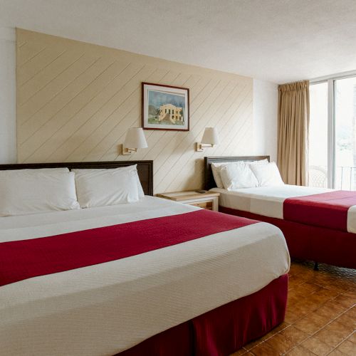 The image shows a hotel room with two double beds, a painting above, and a sliding glass door leading to the outside.